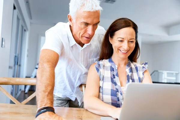 Heureux couple d'âge mûr moderne travaillant sur ordinateur portable à la maison — Photo