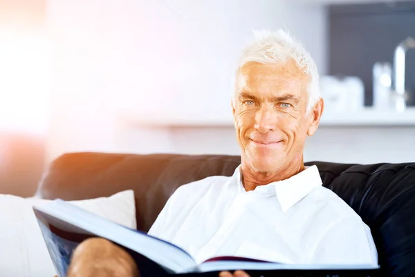 Hezký sennior muž čte knihu relaxační na pohovce — Stock fotografie
