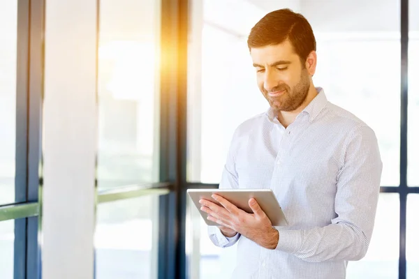 Joven hombre de negocios guapo usando su touchpad de pie en la oficina — Foto de Stock