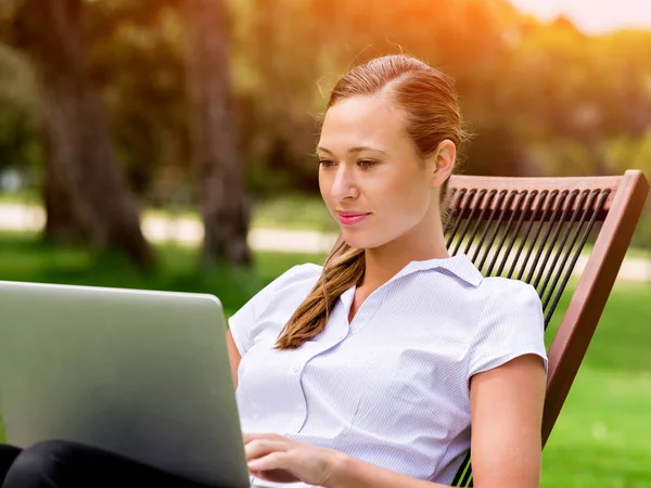 若いビジネス女性の公園で座っていると、ノート パソコンでの作業 — ストック写真