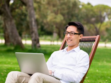 Genç işadamı açık havada otururken dizüstü bilgisayar kullanarak