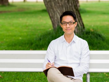 Bankta oturan ve Not Defteri'nde yazma çekici düşünceli işadamı