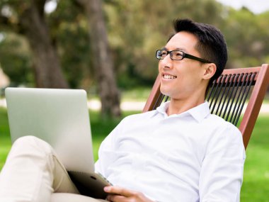 Genç işadamı açık havada otururken dizüstü bilgisayar kullanarak