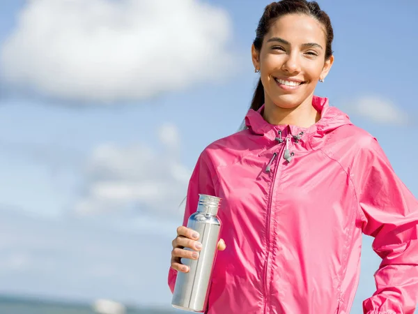 Schönes Mädchen in Sportkleidung trinkt Wasser nach dem Training am Strand — Stockfoto