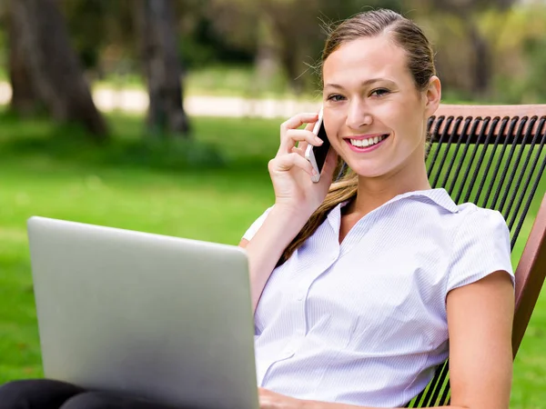 Młoda kobieta siedzi w parku i praca z laptopem — Zdjęcie stockowe