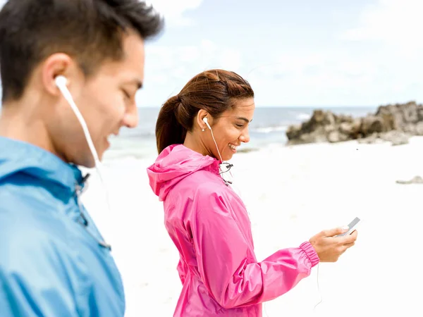 Sporty young couple with earphones on the sea coast — Stock Photo, Image