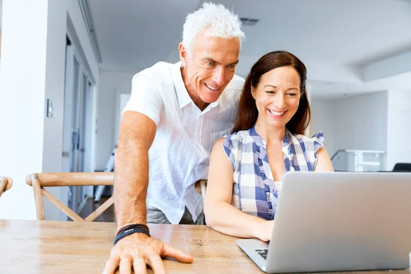 Heureux couple d'âge mûr moderne travaillant sur ordinateur portable à la maison — Photo