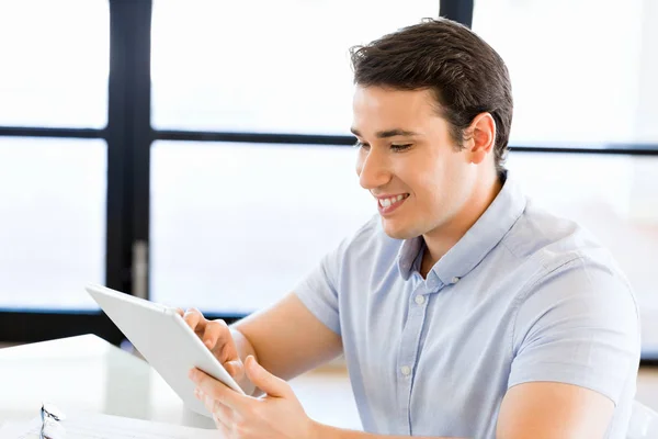 Jonge knappe zakenman met zijn touchpad zitten in kantoor — Stockfoto