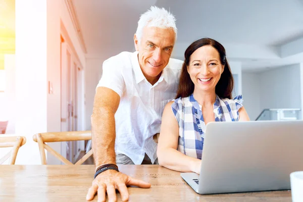 Heureux couple d'âge mûr moderne travaillant sur ordinateur portable à la maison — Photo