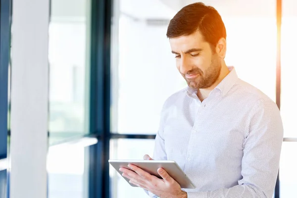 Joven hombre de negocios guapo usando su touchpad de pie en la oficina — Foto de Stock