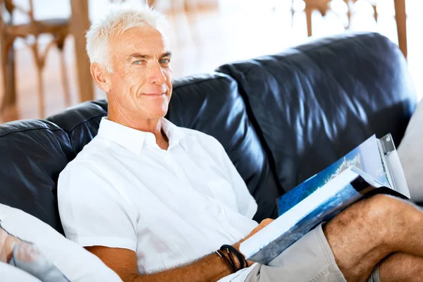 Bello sennior uomo che legge un libro rilassante su un divano — Foto Stock