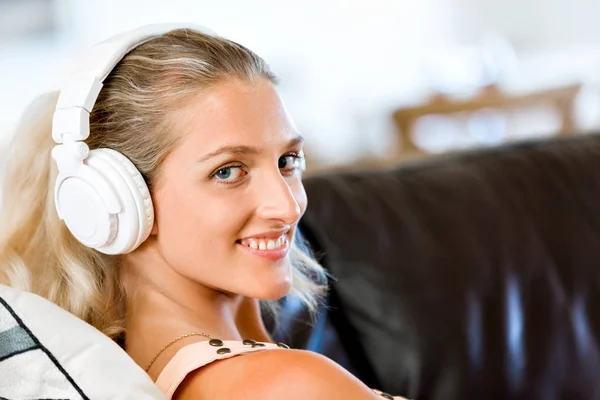 Jovem mulher sorridente com fones de ouvido relaxando no sofá ouvindo música online usando um smartphone — Fotografia de Stock
