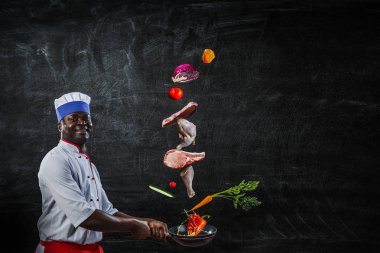 Siyah adam önlük giyiyor ve yemek pişiriyor. Karışık ortam