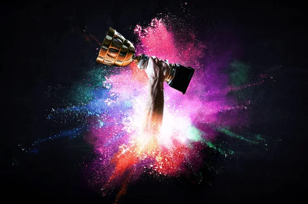 Hands holding champion cup on colourful splashes background. Mixed media — Stock Photo, Image