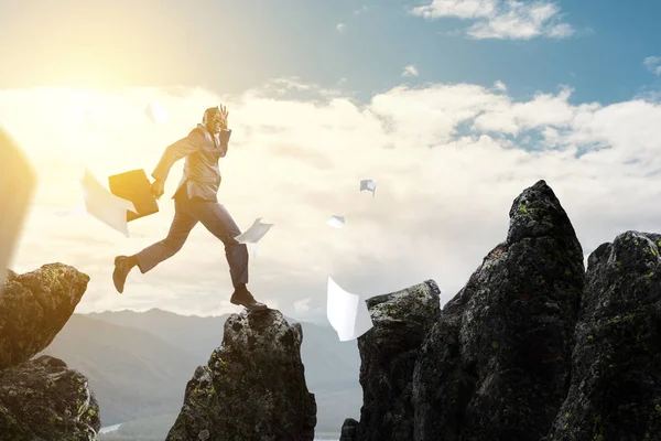 Vista lateral de un hombre de negocios negro saltando sobre piedras de montaña — Foto de Stock