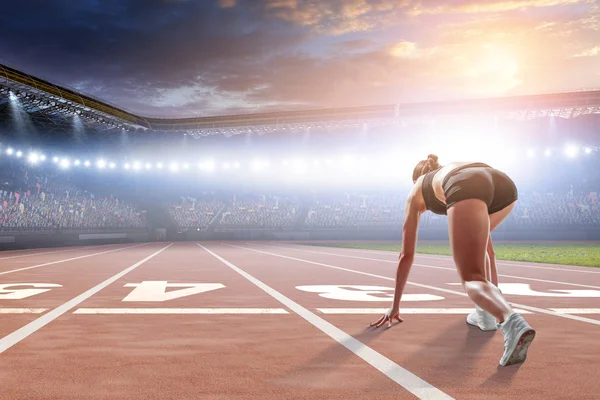 Mulher velocista começar a posição pronta em um estádio — Fotografia de Stock