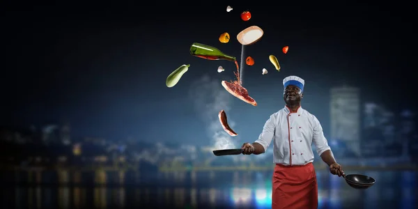 Black man wearing an apron and cooking in action. Mixed media — Stock Photo, Image