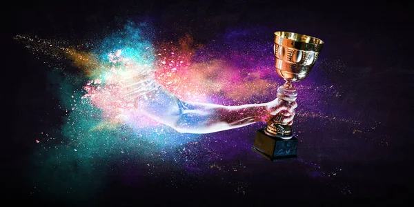 Hands holding champion cup on colourful splashes background. Mixed media — Stock Photo, Image