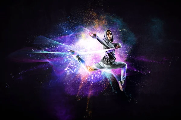 Современная танцовщица прыгает в толстовке с красочными брызгами на заднем плане. Смешанные медиа — стоковое фото
