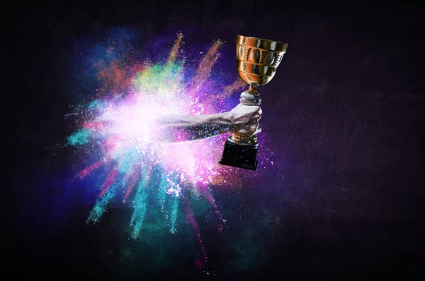 Hands holding champion cup on colourful splashes background. Mixed media — Stock Photo, Image