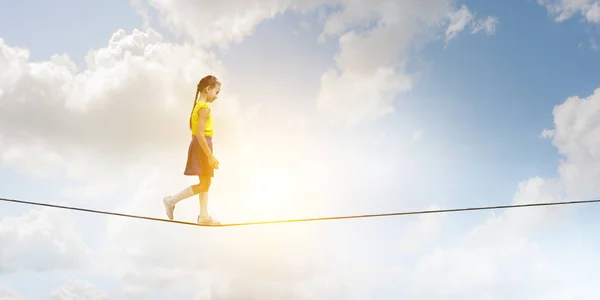 Cute joyful little girl walking on a rope over city. Mixed media — Stock Photo, Image