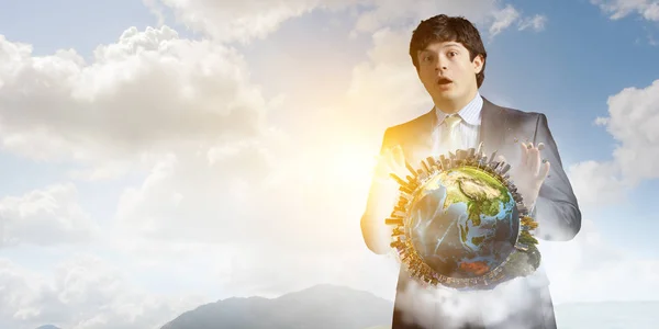 Young businessman standing surprised and holding Earth model. Mixed media — Stock Photo, Image