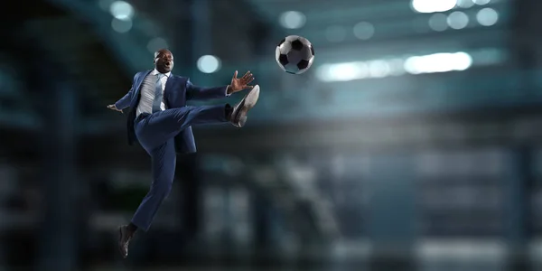 Black businessman in a suit playing footbal