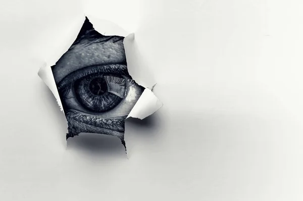 Ojo en un agujero de papel roto —  Fotos de Stock