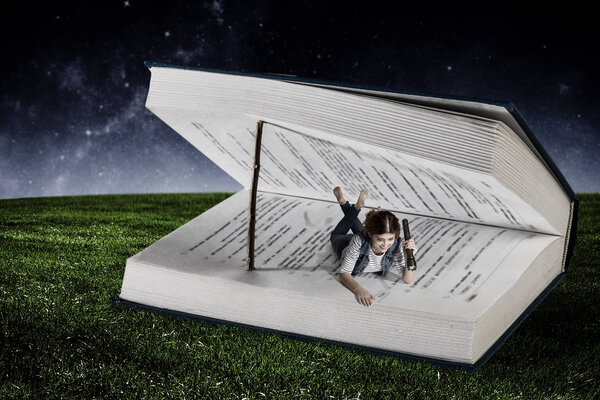 Little woman lying in a large book opened with wooden natural bookmark