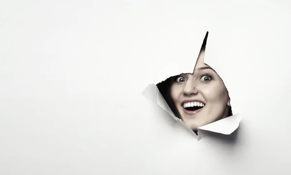 Mulher olhando para fora de um buraco de papel rasgado — Fotografia de Stock
