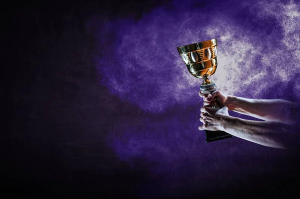 Hand holding up a gold trophy cup against dark background — Stock Photo, Image