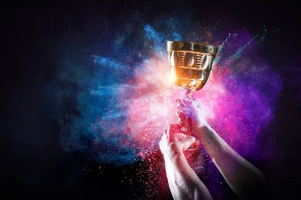 Hand holding up a gold trophy cup against dark background — Stock Photo, Image