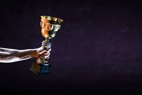 Mão segurando uma taça de troféu de ouro contra fundo escuro — Fotografia de Stock