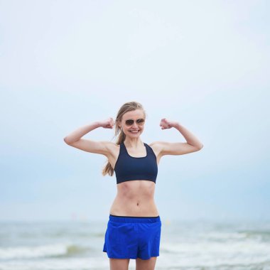Sağlıklı fitness koşucu kız onun pazı gösterilen güneş gözlüğü takıyor. Genç Avrupalı Bayan plaj kardiyo eğitim egzersiz sırasında bir dinlenme alarak