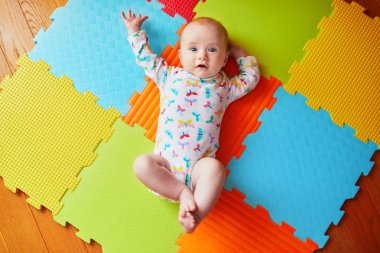 4 months old baby girl lying on colorful play mat on the floor. Activity carpet for kids clipart