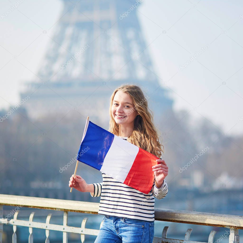 Beautiful young girl with French national tricolor flag near the Eiffel tower