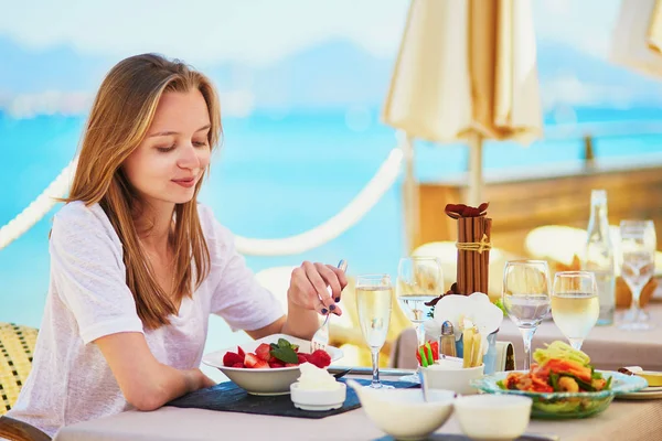 美しい若い女性はシャンペンを飲んで ビーチのレストランで彼女の休暇の 海の中に果物を食べる — ストック写真
