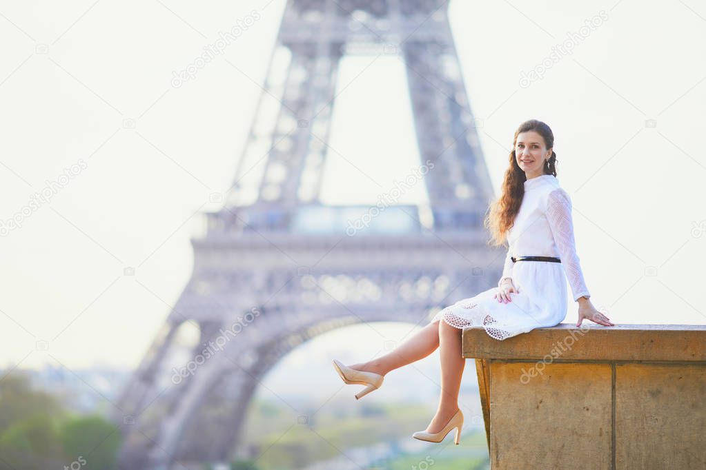 Happy young woman in white dress near the Eiffel tower in Paris, France