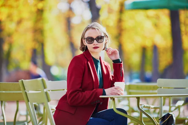 明るい日当たりの良い秋の日に公園でコーヒーを飲みながらエレガントなパリの女性 — ストック写真