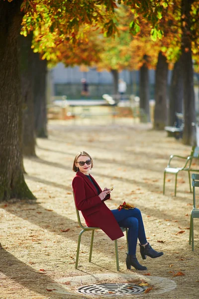 优雅的巴黎妇女使用她的手机在公园的一个灿烂的阳光明媚的秋天天 — 图库照片