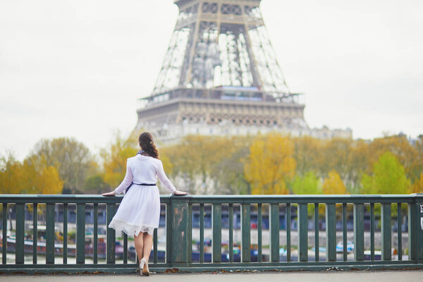 Happy young woman in white dress near the Eiffel tower in Paris, France