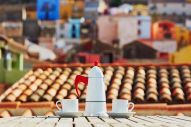 Coffemaker and two cups of fresh espresso coffee on a table of restaurant, cafe or terrace with view to Bosa village, Sardinia, Italy clipart