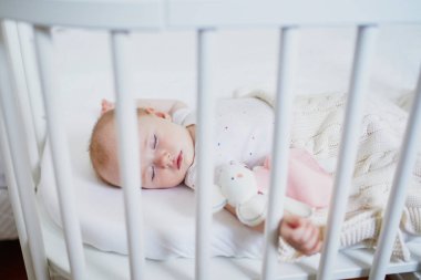 Sevimli bir kız bebek, anne babasının yatağına bağlı olarak birlikte yattığı karyolada uyuyor. Küçük çocuk karyolada kestiriyor. Güneşli kreşte küçük bir çocuk.
