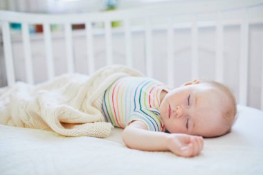 Sevimli bir kız bebek, anne babasının yatağına bağlı olarak birlikte yattığı karyolada uyuyor. Küçük çocuk karyolada kestiriyor. Güneşli kreşte küçük bir çocuk.