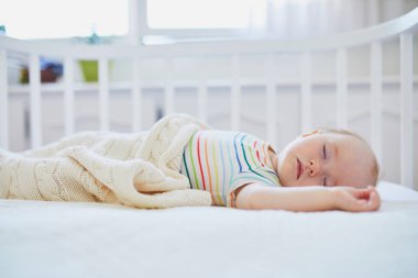 Sevimli bir kız bebek, anne babasının yatağına bağlı olarak birlikte yattığı karyolada uyuyor. Küçük çocuk karyolada kestiriyor. Güneşli kreşte küçük bir çocuk.