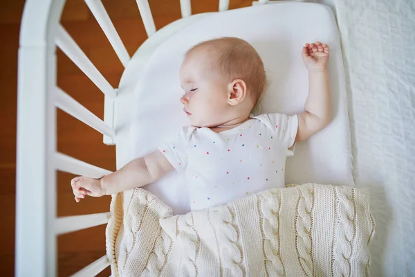 親のベッドに付属の共同寝台ベビーベッドで寝ている愛らしい赤ちゃんの女の子 小さな子供がベッドで一日昼寝をしている 日当たりの良い保育園の幼児 — ストック写真