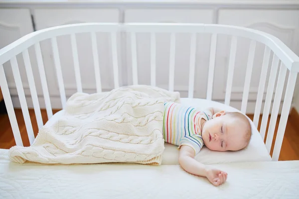 Adorable baby girl sleeping in co-sleeper crib attached to parents\' bed. Little child having a day nap in cot. Infant kid in sunny nursery