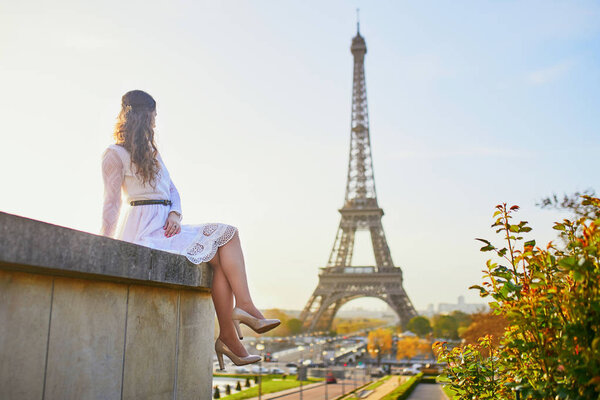 Happy young woman in white dress near the Eiffel tower in Paris, France