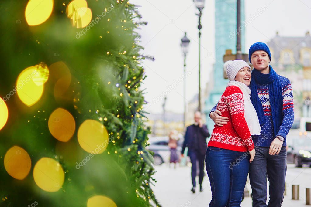 Happy couple in colorful sweaters walking on a street of Paris decorated for Christmas