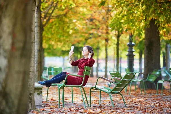 美しい若い女性明るい秋の日 パリのチュイルリーの庭で彼女の携帯電話で Selfie を撮影します 観光と秋のシーズンにフランスの休暇 — ストック写真